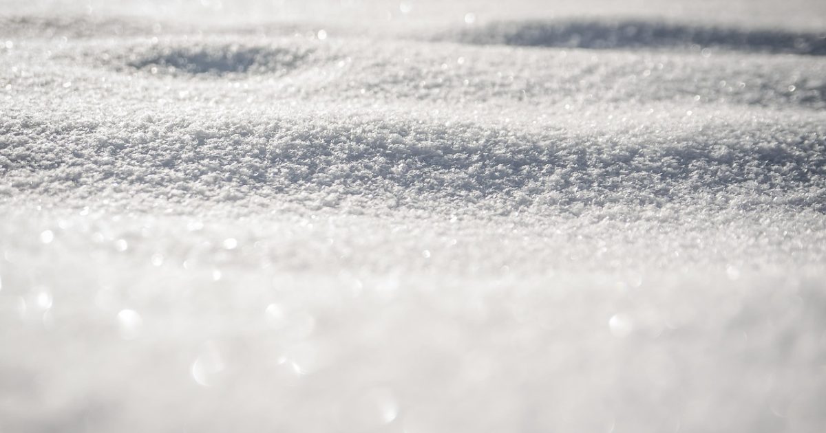 北疆就业冬季城市街景，行人穿着厚外套走在积雪的人行道上，路边暖黄色路灯与远处楼宇灯光交织